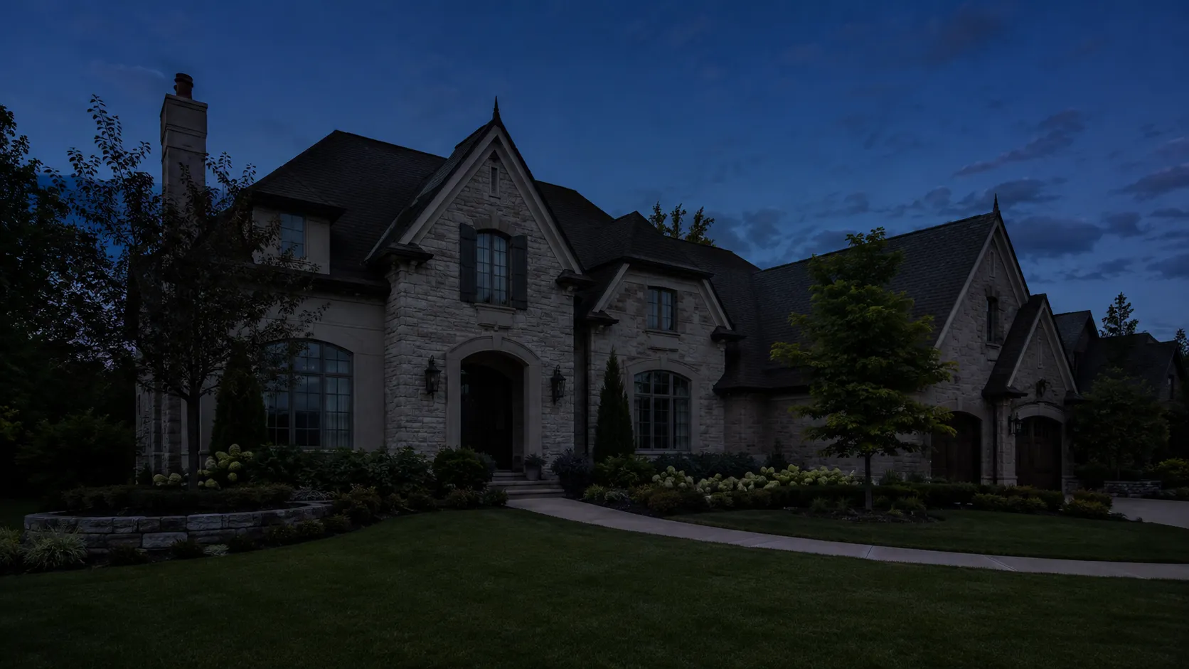 A stone Tudor-style home at dusk, before holiday lighting